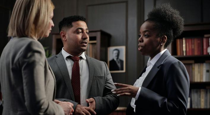 A man and two women all in suits in a conversation in an office.